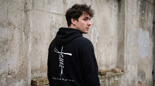 Junger Mann von hinten mit christlichem Hoodie mit Rückenprint an einer Betonwand