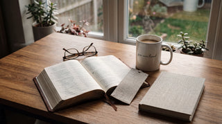 Offene Bibel und eine christliche Tasse auf einem Holztisch im Morgenlicht