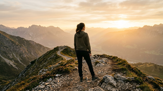 Person auf einem Bergrücken bei Sonnenaufgang als Symbol für Kraft und Zuversicht